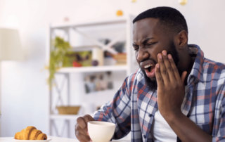 Image of man holding his cheek from dental pain with coffee cup in hand